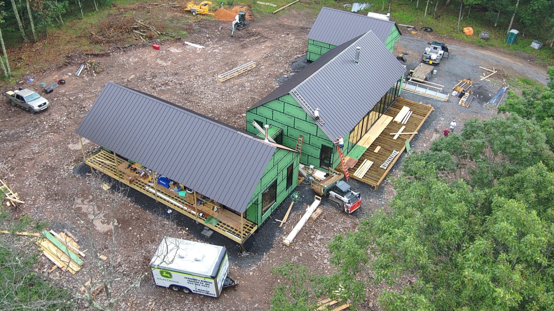 Aerial view of a current build — three connected structures with standing-seam metal roofs on a wooded lot